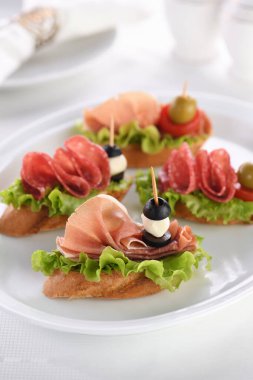 Yaprak salatalı, salamlı ya da Parma jambonlu, domatesli, mozzarella ve zeytinli yumuşak baget kanepeleri. Partide çeşitli tabaklar var..