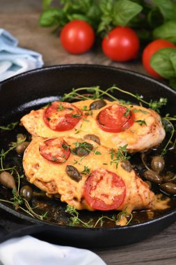 Tender chicken breast baked with tomatoes, capers, herbs under cheese crust in a frying pan