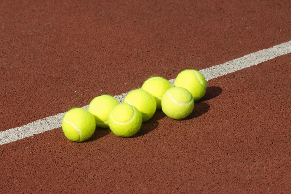 Line of seven yellow tennis balls red on court — Stock Photo, Image