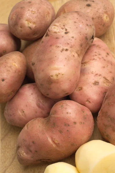 Patatas peladas y sin pelar en primer plano de tablero de cocina de madera — Foto de Stock