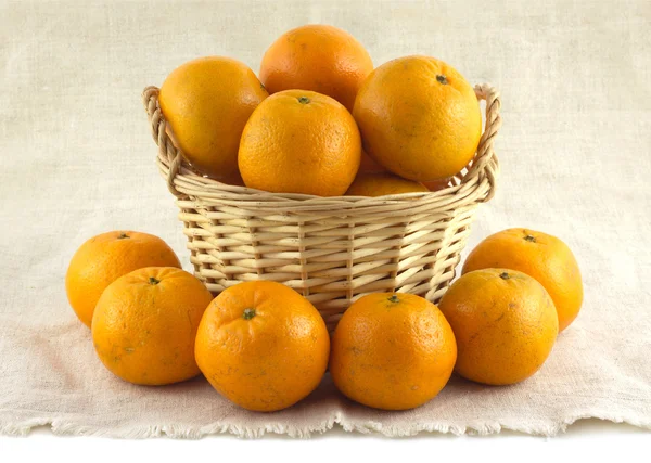 Many ripe oranges in brown wicker basket and near it isolated — Stock Photo, Image