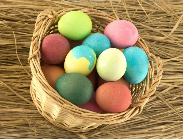 Color Easter eggs in brown basket on straw closeup — Stock Photo, Image