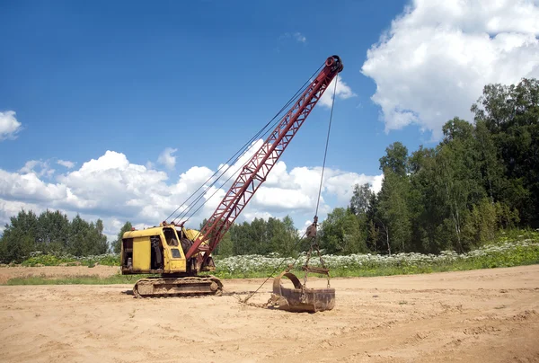 Excavadora amarilla con gran cubo pesado de pie sobre arena sobre fondo de bosque y cielo azul claro —  Fotos de Stock