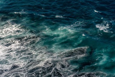 Deniz köpüğü ve dalgalı okyanus suyu yüzeyi, hava manzaralı. Mavi-yeşil, açık deniz ve yeşil renkli karışık renklerde soyut deniz arkaplanı.