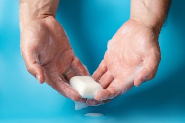 Küresel Temizlik Günü, kişisel temizlik konsepti. Köpüklü bir adamın eli mavi bir arka planda sabun tutar..