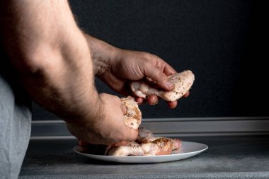 Bir adam tavuk kanatlarını pişirmek için baharatlarla ovalıyor..