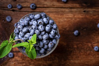 Koyu ahşap zemin üzerinde cam bir kasede nane yapraklı taze yaban mersini..
