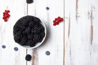 Taze böğürtlenler beyaz ahşap arka planda bir tabakta.