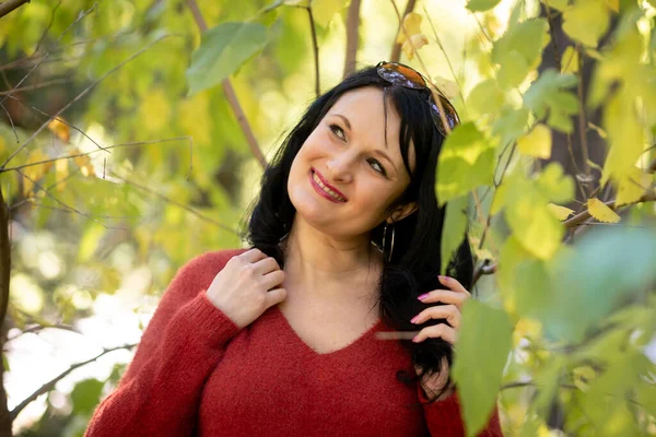 一位黑发女子在绿树旁的公园里笑着 穿着红色毛衣 — 图库照片