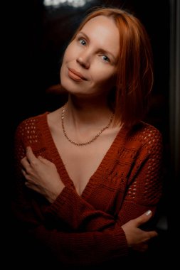 40 'lı yaşlarındaki çekici bir kadın karanlık bir arkaplanda kameraya bakıyor..