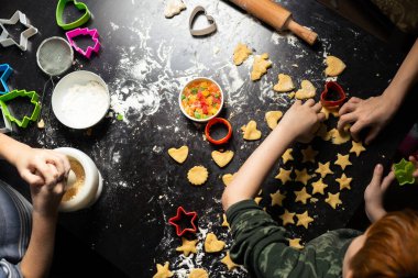 Çocuklar karanlık bir mutfak masasında yıldız şeklinde doğum günü kurabiyeleri hazırlıyorlar. Evdeki mutfakta ortak aile aktivitesi. Yukarıdan görüntüle.