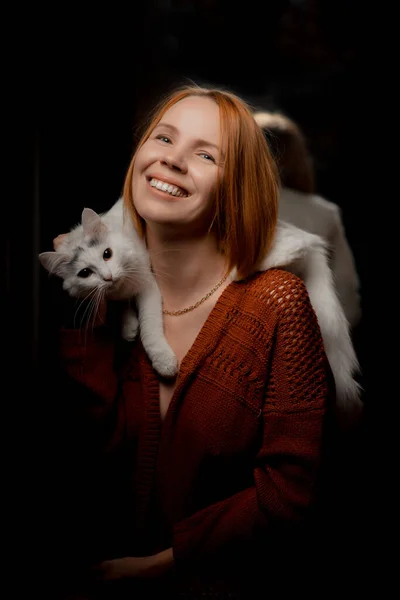 一位肩上背着白猫的中年妇女在黑暗的背景下微笑着 — 图库照片