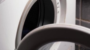 Bir adam çamaşır makinesine çamaşır koyuyor..