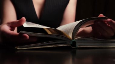 Kadın karanlık bir odada bir kitap sayfasını çeviriyor..