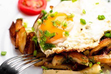 Yumurtalı kızarmış patates, sıvı sarısı, otlar ve domatesler beyaz tabakta..