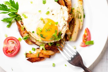 Yumurtalı kızarmış patates, otlar ve domatesler beyaz bir tabakta, ahşap arka planda..