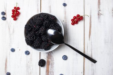 Taze böğürtlenler beyaz ahşap arka planda bir tabakta.