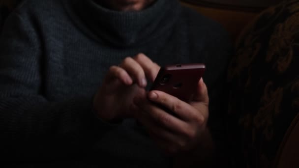 暖かいセーターの認識できない男が家でソファの上の携帯電話に入力されています — ストック動画