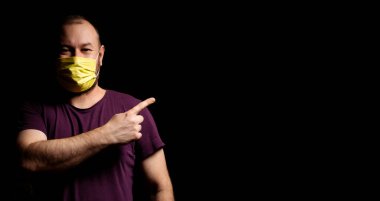 Tıbbi maskeli bir adam boş bir noktayı işaret ediyor. Metnin için yer.