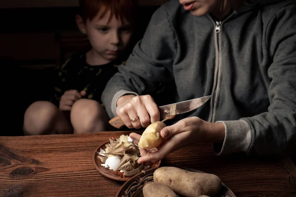 Annesi Olan Bir Çocuk Koyu Bir Zeminde Patates Soyar Bir — Stok fotoğraf