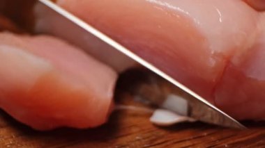 Çiğ tavuk filetosunu tahta arka planda yakın plan bıçakla kes..