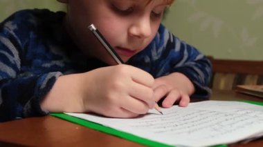 Genç bir çocuk ödevlerini yapar ve kalemle deftere yazar..