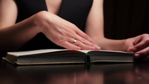 暗い部屋のテーブルの上に寝そべっている聖書を読む女性 — ストック動画