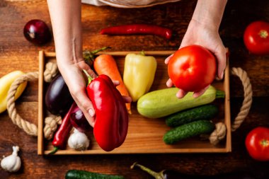 Tanınmayan bir kadın elinde farklı sebzelerin arka planında domates tutuyor. Sağlıklı gıda ve vejetaryenlik kavramı.