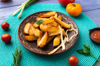 Tabakta büyük parçalar halinde patates kızartması. Masada turkuaz peçete ve farklı sebzeler var..