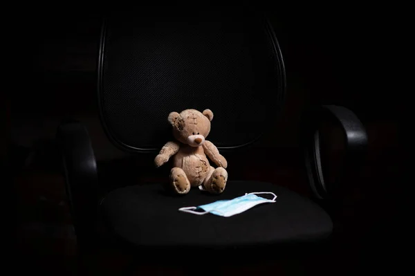 Teddybär Und Medizinische Maske Auf Einem Bürostuhl Auf Schwarzem Hintergrund — Stockfoto