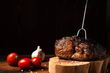 Ahşap tezgahta pişmiş bir parça et ve çiğ sebze. Baharatlı fırında pişirilmiş domuz ya da sığır eti..
