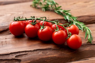 Ahşap arka planda kiraz domatesleri ve biberiye. Taze domates dalı. Vejetaryen yemeği..