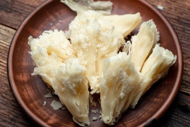 Ahşap bir zeminde, kil tabakta dilimlenmiş sert peynir cipsi..