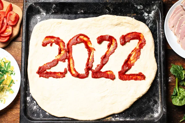 2022 numara hamurda ketçap ile yazılmış. Pizza pişiriyorum. Yeni yılın mutfak konsepti..