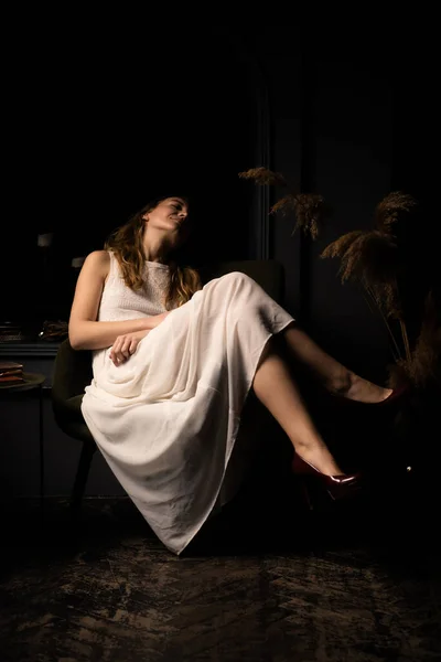 Beyaz Elbiseli Genç Bir Kadın Karanlık Bir Odada Koltukta Rahatça — Stok fotoğraf