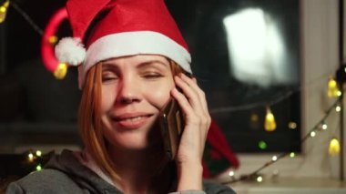 Yılbaşı şapkasıyla 40 yaşında orta yaşlı bir kadın cep telefonunda gülümsüyor. Yeni yıl, Noel selamları.