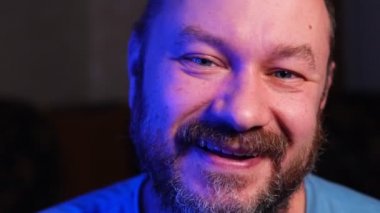 Sıradan traşsız bir adam yakından gülümsüyor ve kameraya bakıyor..