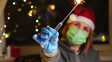 Yeni yıl tatili ve aşı konsepti. Bir kadının elinde yanan maytap olan tıbbi bir şırınga..