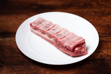 Tahta arka planda beyaz tabakta taze çiğ et ve domuz pirzolası..