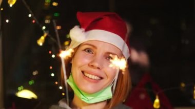 Yeni yıl tatili ve karantina konsepti. Elinde maytap olan, sönük tıbbi maskeli bir kadın..