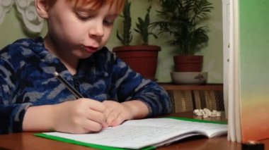 Genç bir çocuk ödevlerini yapar ve kalemle deftere yazar..
