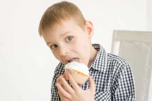 A young boy in a shirt eats a cake on a light background. The food joy of sweets.