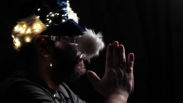 新年の帽子を被った髭の男が暗闇の中で祈る — ストック動画