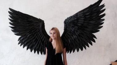 Siyah melek kanatları ve beyaz arka planda siyah elbisesi olan bir kız..