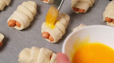 Çiğ yumurta sarısı ve sosisli çöreklerle kaplı. Pişirme için hazırlanılıyor.