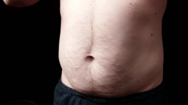 Bir adamın şişman karnı karanlık bir arka planda dönüyor. Obezite, kilo sorunları. Diyet zamanı, spor konsepti.