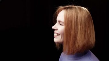 Kadın güler ve yüzünü çevirir. Profil görünümü. Mesajın için yer aç. Karanlık arka plan. Kırk yaşında kızıl saçlı bir kadın. Mutlu yüz..