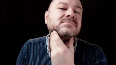 Orta yaşlı bir adam aşırı büyümüş sakalını okşar. Karanlık arka plan. Sakal bakımı.