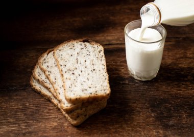 Tohumlu ve sütlü ekmek parçaları bir bardağa dökülüyor. Koyu ahşap arka plan. Sabah kahvaltısı. Sağlıklı yemek..