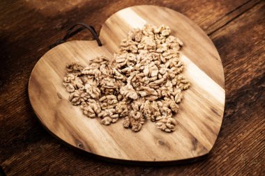 Soyulmuş ceviz. Kalp şeklinde ahşap bir tahtanın üzerinde. Sağlıklı yiyecekler. Doğal arkaplan.